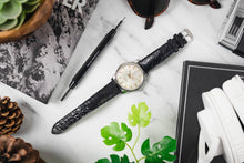 Load image into Gallery viewer, Black longines watch wristwatch with white face on a marble surface with plants and stationery items.
