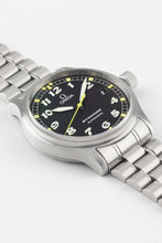 Load image into Gallery viewer, A close-up, angled view of the Omega Dynamic watch face resting on a white surface, highlighting the texture of the black dial, the luminescent hands, and the brushed finish of the stainless steel case.