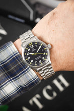 Load image into Gallery viewer, A close-up of the watch being worn on a wrist, paired with a blue and white plaid flannel shirt, showing how the 36mm case sits on the arm.