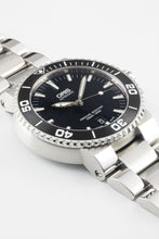 Load image into Gallery viewer, A close-up, angled studio shot of an Oris Aquis Date watch, highlighting the matte black ceramic bezel, black dial with luminous markers, and the brushed finish of the stainless steel lugs.
